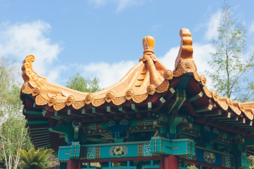 Japanese style golden coloured rotunda roof with trees, blue sky and clouds in the background