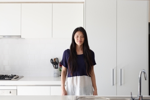 Japanese woman standing in kitchen with eyes closed