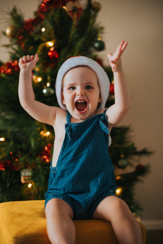 Joyful blonde girl laughs with her hands in the air by a Christmas tree - Australian Stock Image