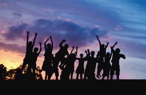 Jumping people on a hilltop silhouetted at sunset - Australian Stock Image