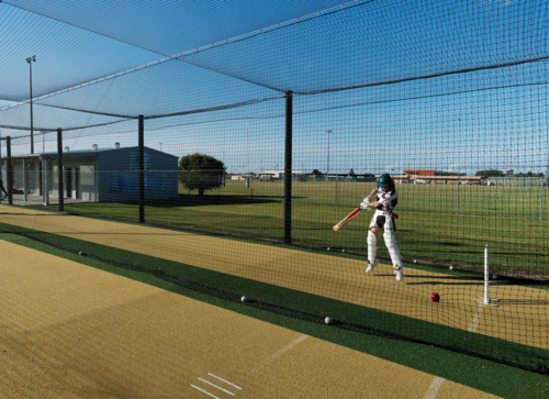 Junior female cricketer striking ball during cricket net training - Australian Stock Image