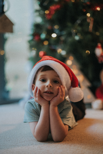 kid in a Santa hat poses by the twinkling Christmas tree - Australian Stock Image