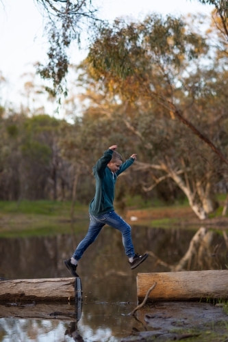 kid jumping between logs on a riverbank - Australian Stock Image