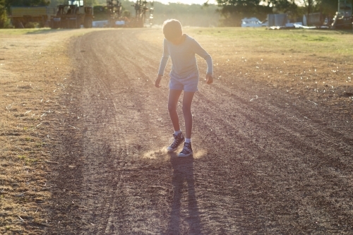 kid kicking up dust on rural farm track - Australian Stock Image