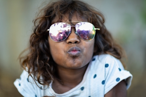 kid making kissing face while wearing mirror sunglasses - Australian Stock Image