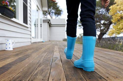 Kid walking along wooden verandah in blue gumboots - Australian Stock Image