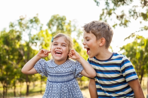 Kids being silly together - boy shouting and roaring at little girl with ears blocked not listening - Australian Stock Image
