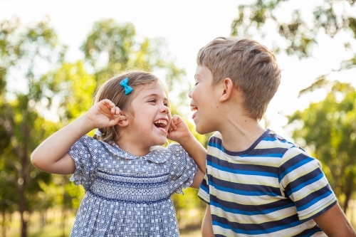 Kids being silly together - boy shouting and roaring at little girl with ears blocked not listening - Australian Stock Image