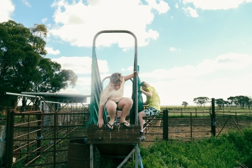 Kids climbing on cattle yard stock ramp on farm - Australian Stock Image