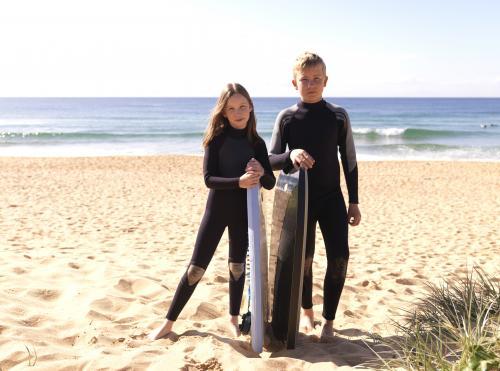 Kids on beach in wetsuits preparing to go body boarding
