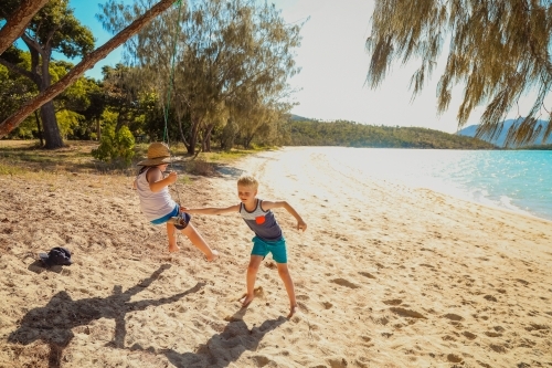 Kids playing on swing on the shore at Dingo Beach in the Whitsundays - Australian Stock Image