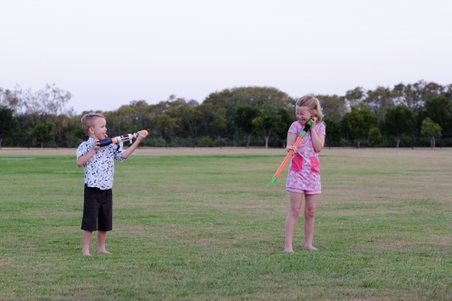 Kids playing with water guns in the park - Australian Stock Image