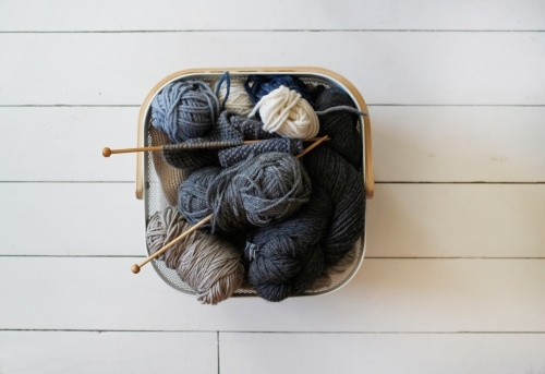 Knitting in white wire basket with wooden knitting needles and grey and cream wool - Australian Stock Image