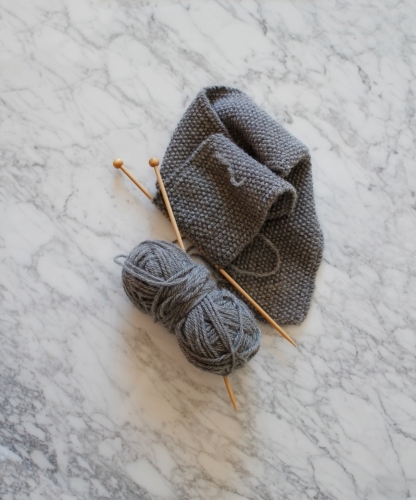 Knitting with wooden knitting needles with grey wool on marble - Australian Stock Image