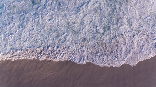 Lacy pattern of water as waves rush over the sand on the beach - Australian Stock Image
