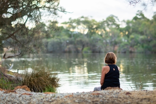 lady sitting by herself on river bank from behind