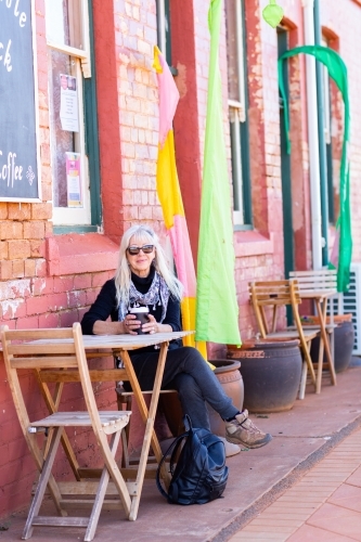 lady sitting on wooden chair outside coffee shop - Australian Stock Image