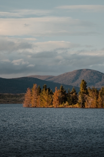 Lake Jindabyne at sunset with autumn coloured trees and mountains - Australian Stock Image