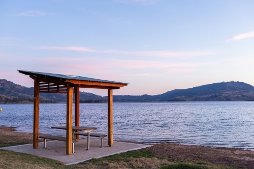 Lakeside picnic bench seating and shelter at dusk with lake and hills - Australian Stock Image