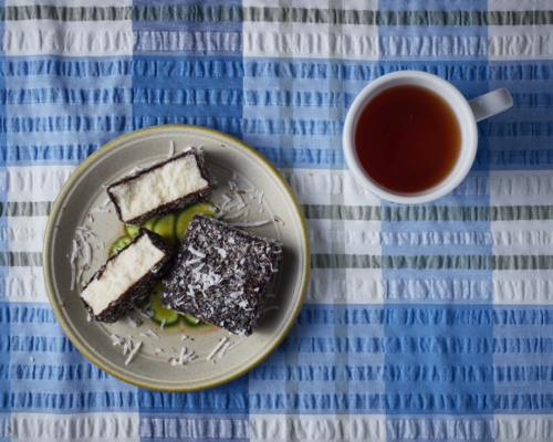 Lamingtons on plate with cup of tea on blue tablecloth. - Australian Stock Image