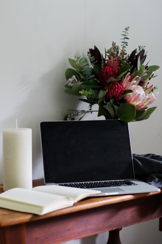 Laptop and notebook on a wooden desk with a bouquet of native flowers