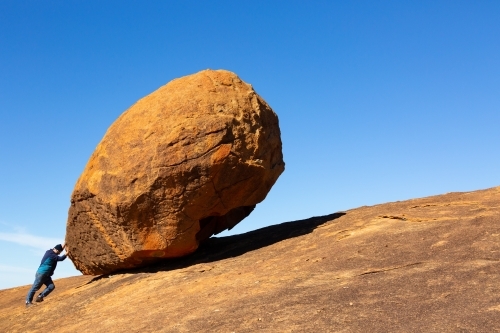 Large granite boulder dwarfs man pretending to push it - Australian Stock Image