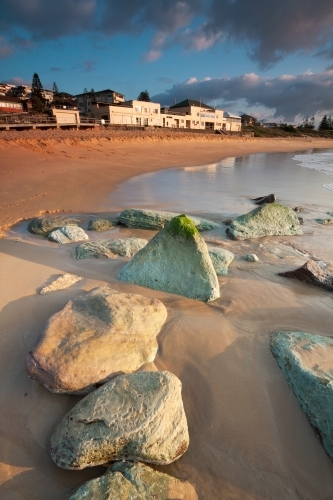 Large rocks embedded in a sandy beach below a surf club building - Australian Stock Image