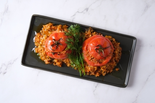 large tomatoes stuffed with rice and green garnish on top - Australian Stock Image