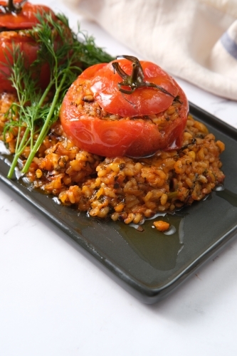 large tomatoes stuffed with rice and green garnish on top - Australian Stock Image