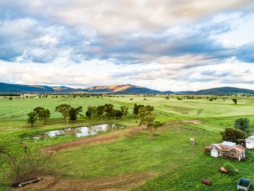 Last sunlight on hills past green farm paddocks and dam - Australian Stock Image