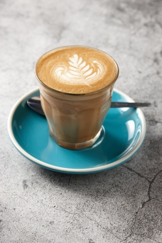 Latte on blue saucer with teaspoon - Australian Stock Image