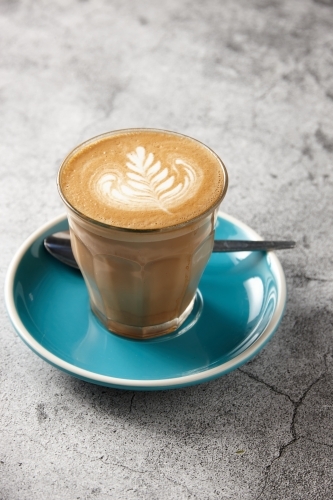 Latte on blue saucer with teaspoon - Australian Stock Image