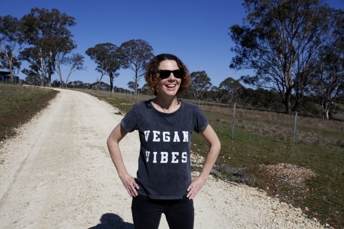 Laughing woman wearing vegan slogan t-shirt standing on rural dirt road - Australian Stock Image