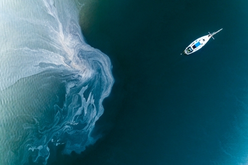 Leachate flowing off tidal mud flats near an anchored yacht.