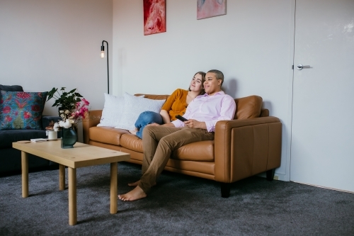 lgbtqi couple sitting on a brown leather couch - Australian Stock Image