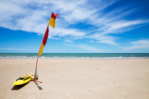 Life saver board and flag on sandy beach