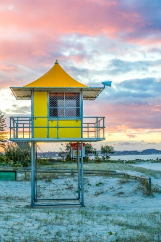 Lifeguard tower on sandy beach against colourful sky