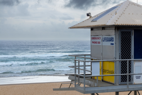 Lifeguard tower on the sand in front of the ocean with an overcast sky - Australian Stock Image