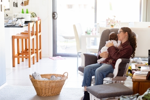 lifestyle image of mother comforting newborn baby to sleep in rocking chair