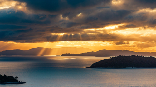 Light Breaking Through Clouds during Sunset over the Whitsundays as seen from Hamilton Island - Australian Stock Image