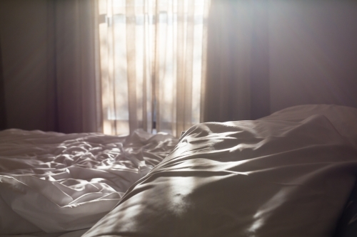 Light through a bedroom window onto a unmade bed
