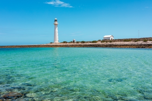 Lighthouse and out buildings on stony land near shallow water - Australian Stock Image
