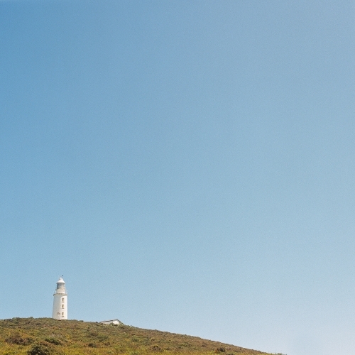 Lighthouse in the distance on a headland with blue sky background