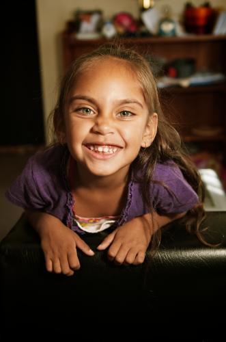 Little Aboriginal Girl on Back of Couch Smiling - Australian Stock Image