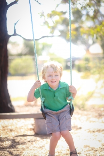 Little blond boy playing on swing at kindergarten - Australian Stock Image