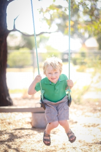 Little blond boy playing on swing at kindergarten - Australian Stock Image