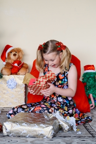 Little blonde girl excitedly looking at a Christmas gift she has just unwrapped - Australian Stock Image