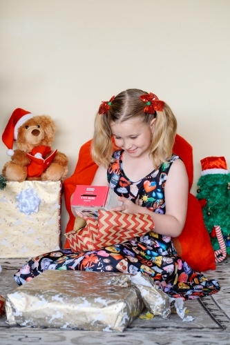 Little blonde girl excitedly looking at a Christmas gift she has just unwrapped - Australian Stock Image