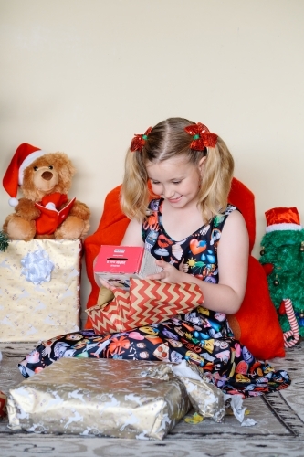 Little blonde girl excitedly looking at a Christmas gift she has just unwrapped