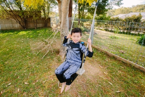 Little boy dressed as batman playing in the garden on a swing on a beautiful day